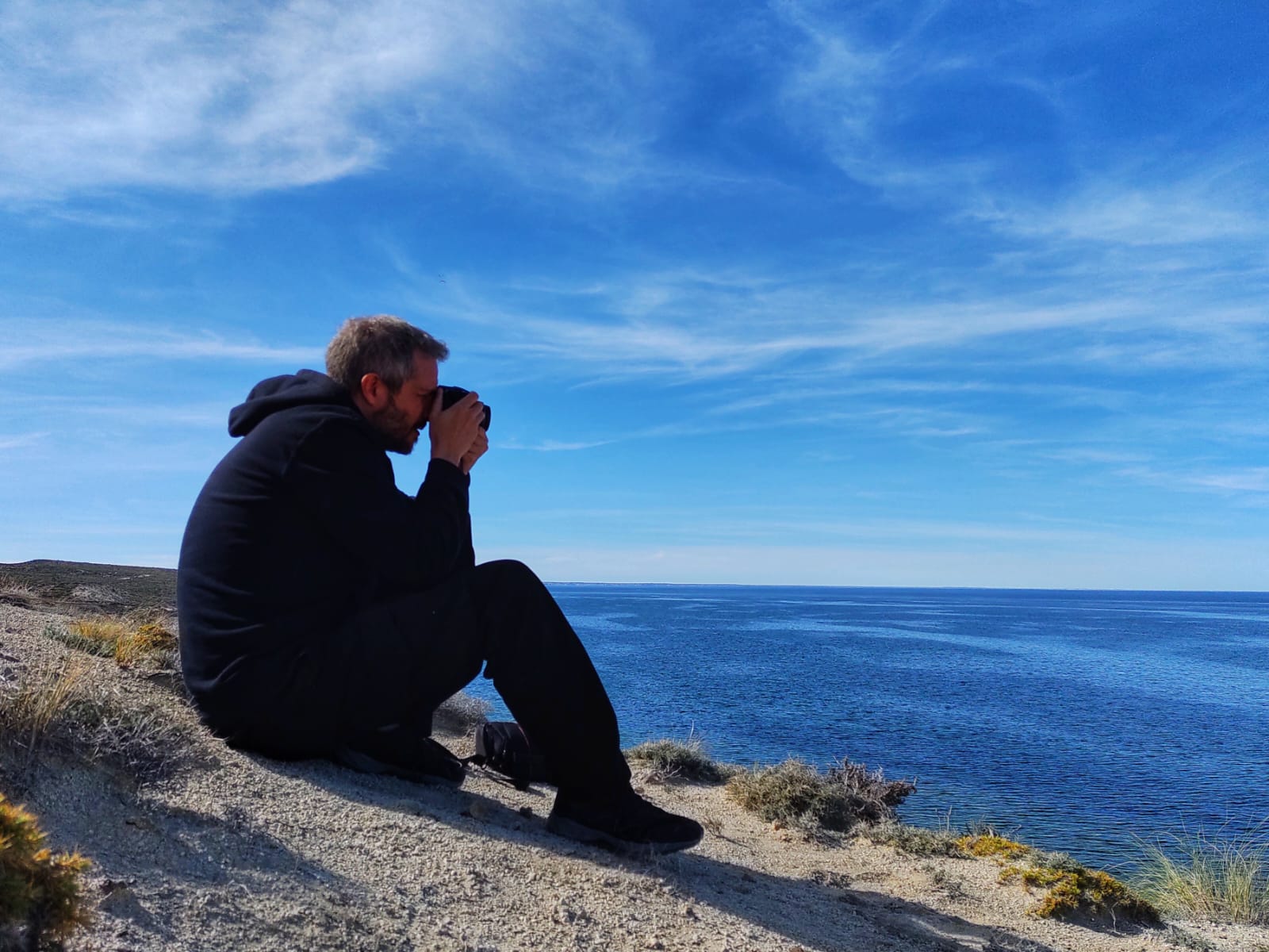 Nelson E. Bolivar seated by the sea taking a photograph